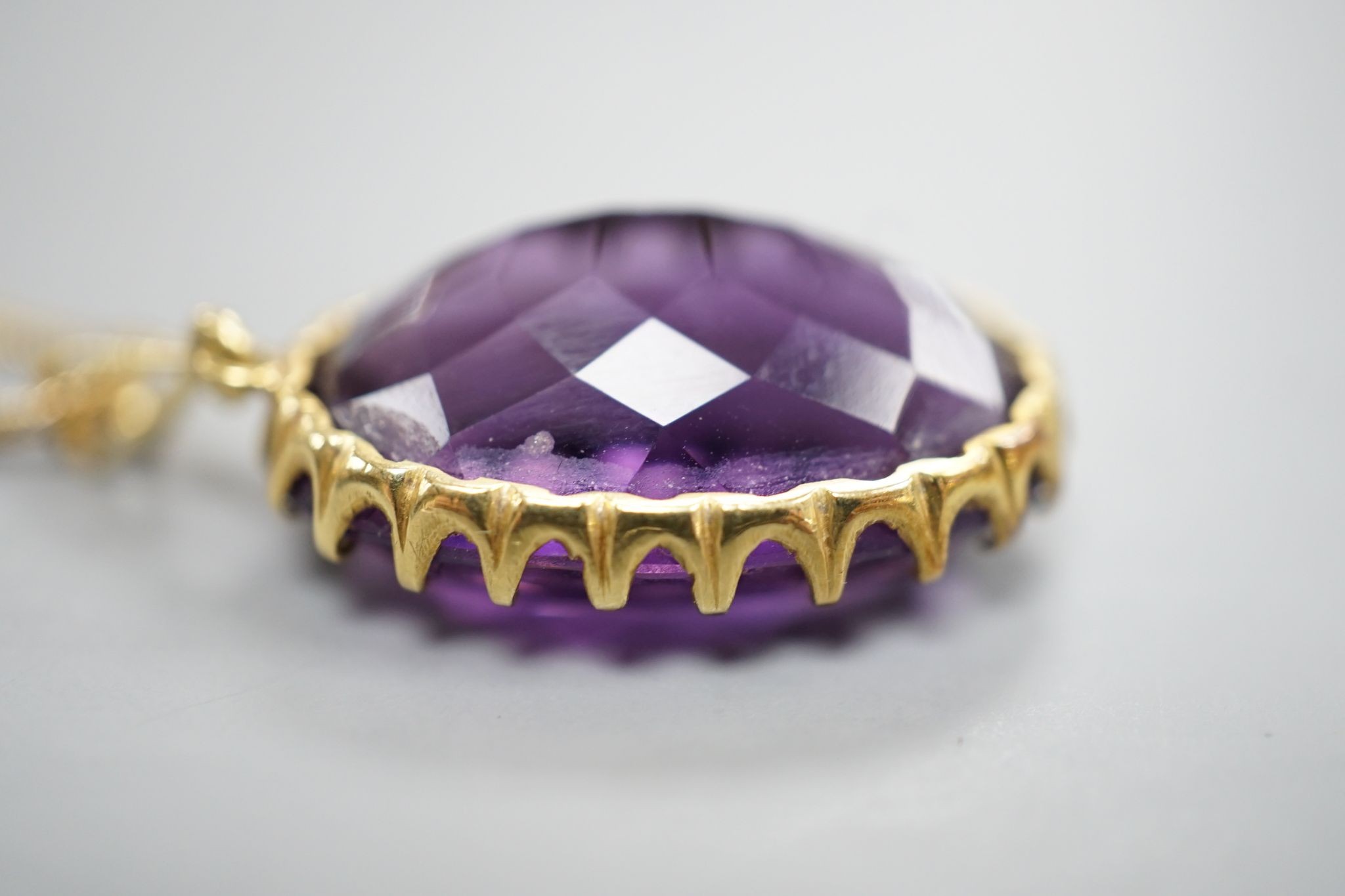 An early 20th century yellow metal mounted oval cut amethyst pendant, overall 37mm, on a yellow metal fine link chain, 49cm, gross weight 10.3 grams.